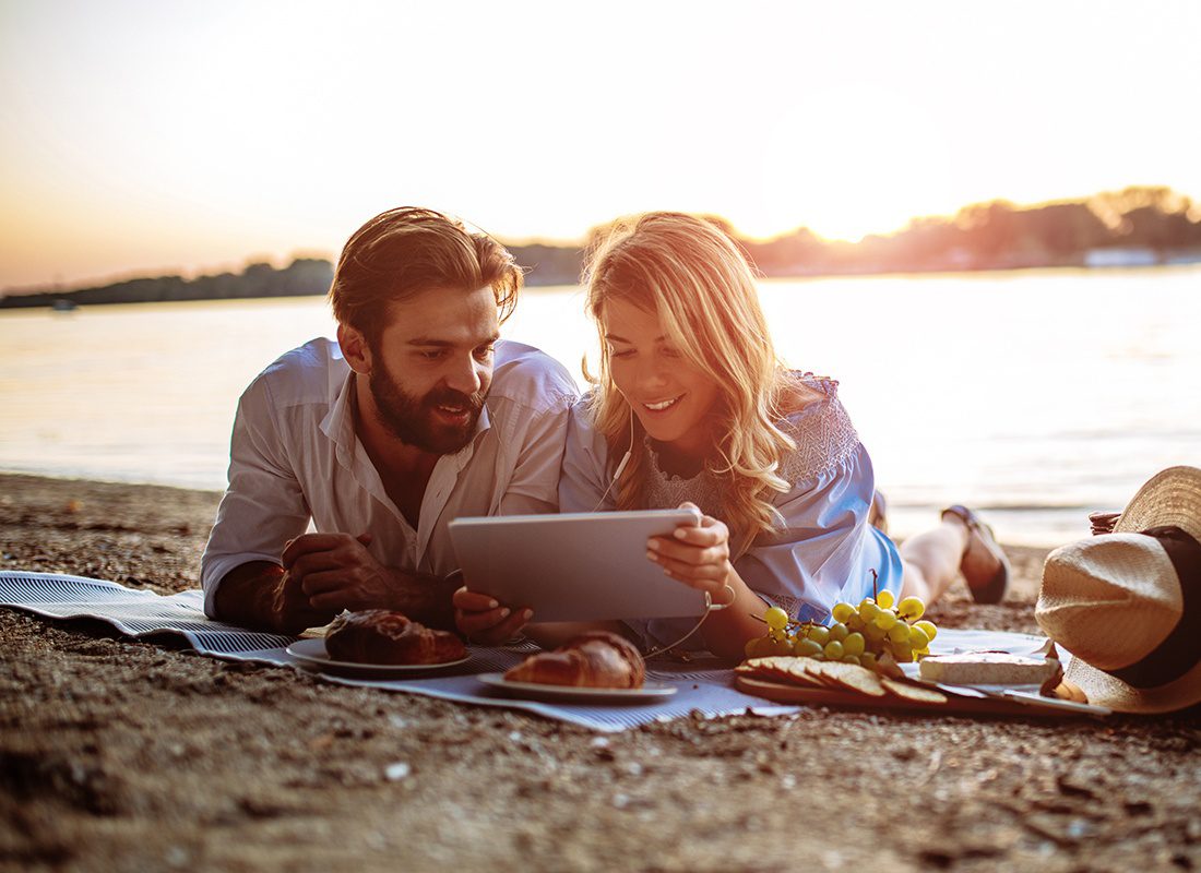 Homepage - Couple Having a Picnic by a Lake Use a Tablet